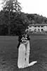 A black and white image of a person dressed as a dog, standing on a lawn with trees and a building in the background.