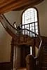 Interior of a building featuring a wooden spiral staircase with a large arched window in the background.