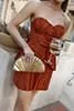 Woman in brown strapless dress holding a gold clutch and a wine glass