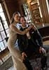A bride in a white dress and a groom in a tuxedo pose together in an elegant, well-lit room with large windows and bookshelves.