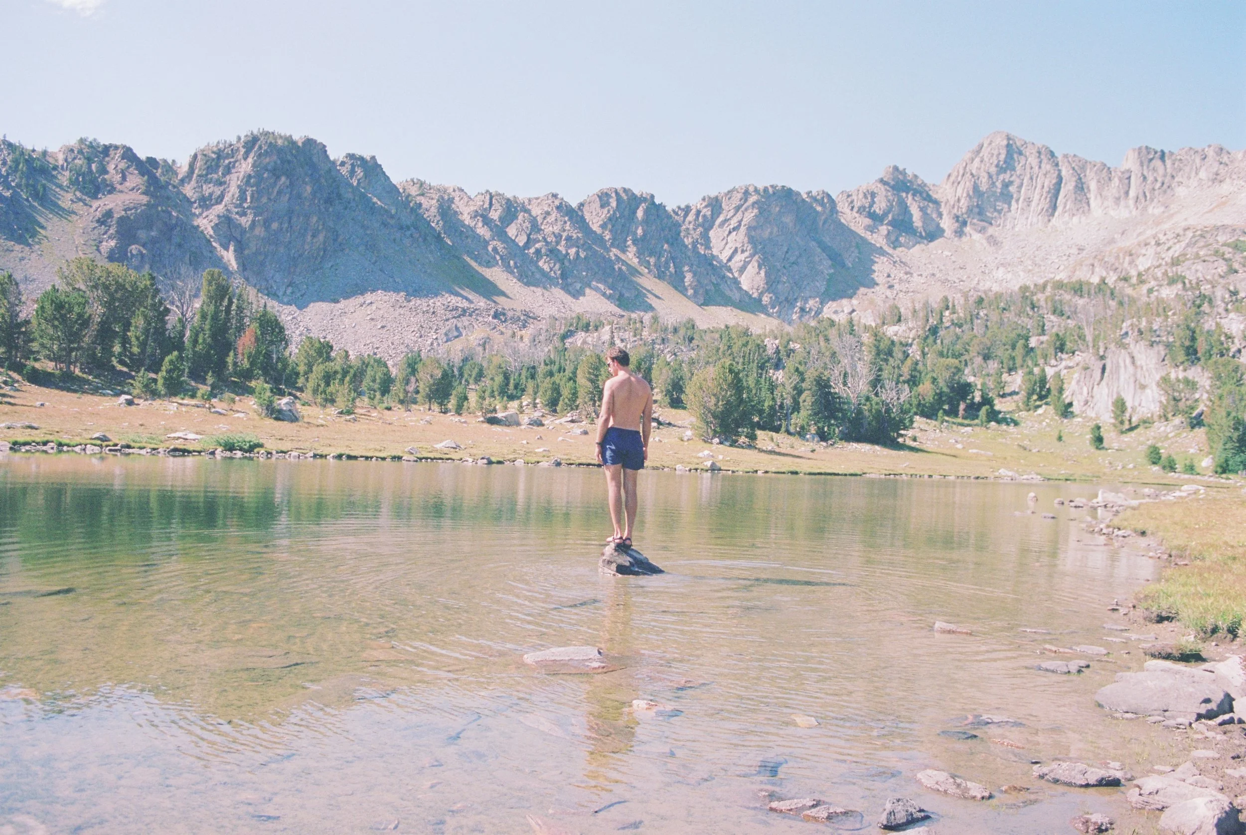 Person standing on a rock in a lake with mountains in the background.