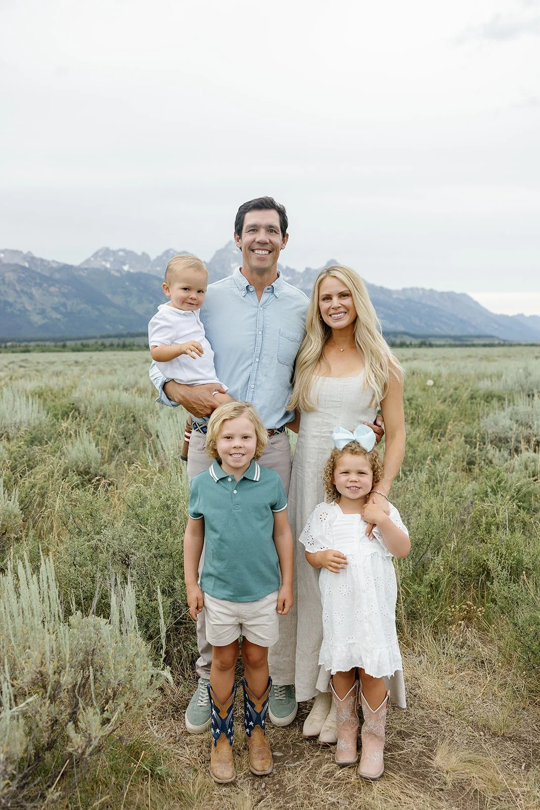 Family of five standing in a field with mountains in the background, smiling at the camera.