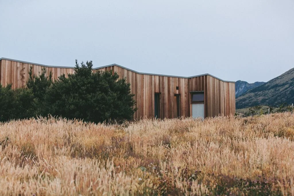 Modern wooden house with angular design in a grassy field, mountain background