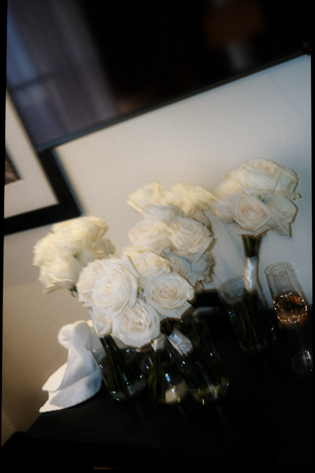 Bouquets of white roses in vases with a champagne glass on the side.
