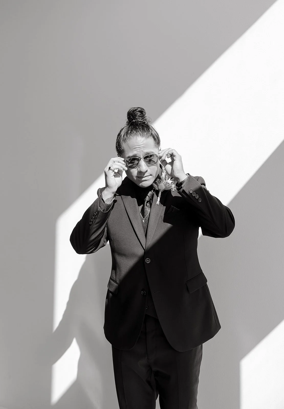 Person in a suit adjusting sunglasses in a bright room with dramatic lighting.