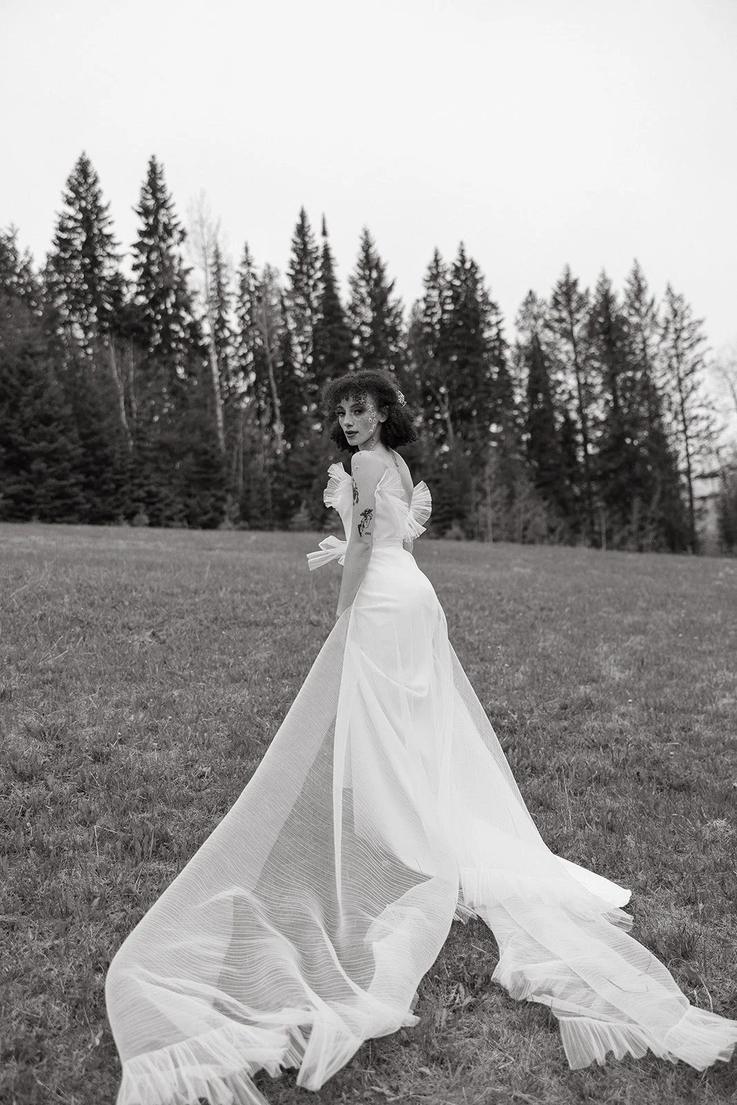 Woman in white dress walking in meadow with trees in background.