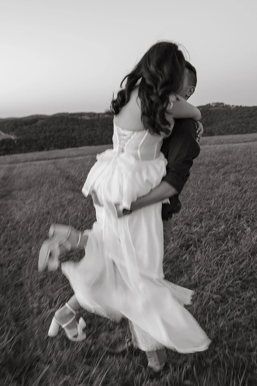 A man lifting a woman in a field, woman wearing a dress, black and white photo