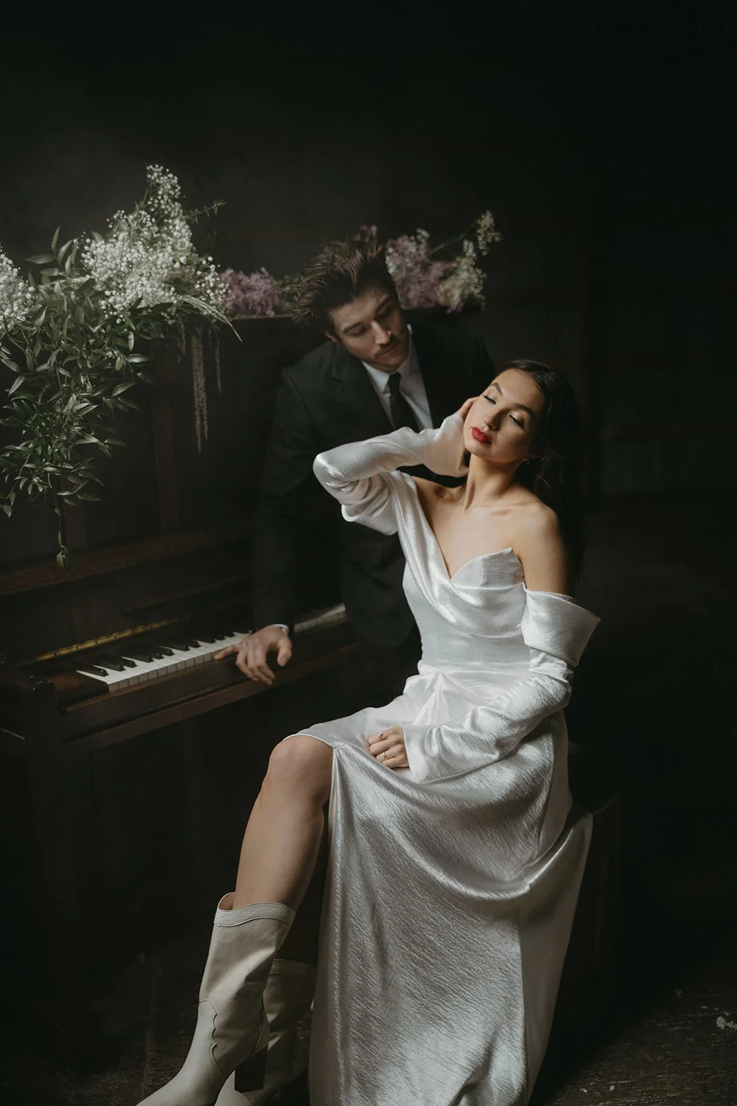 Woman in white dress posing near a man playing a piano with flowers on top