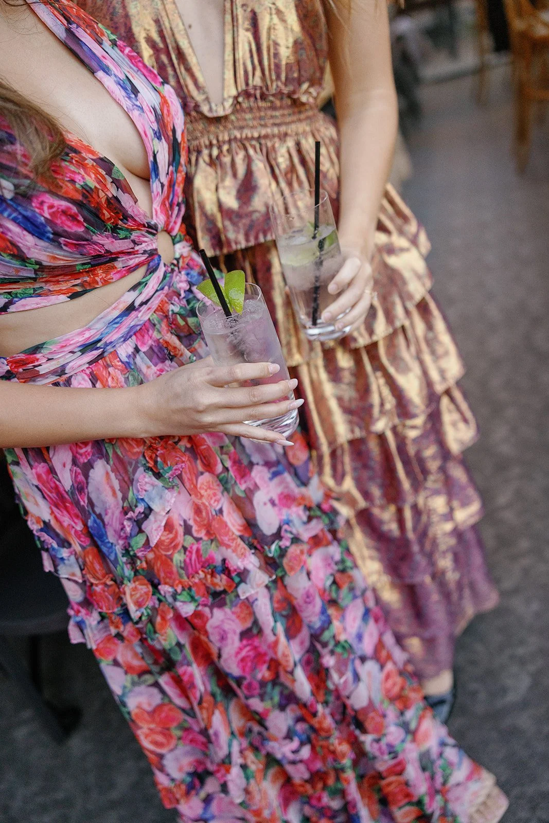 Two women in colorful dresses holding drinks with lime garnish.