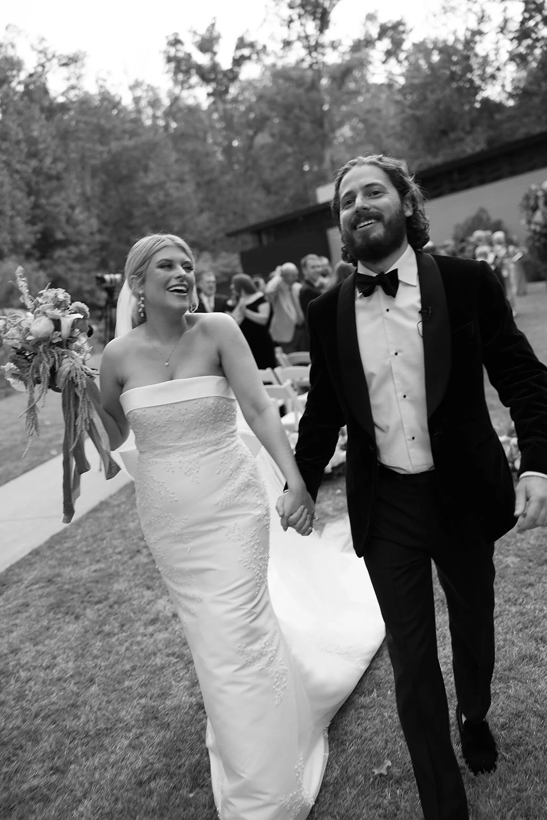 Bride and groom walking hand in hand, surrounded by guests, in an outdoor wedding setting.