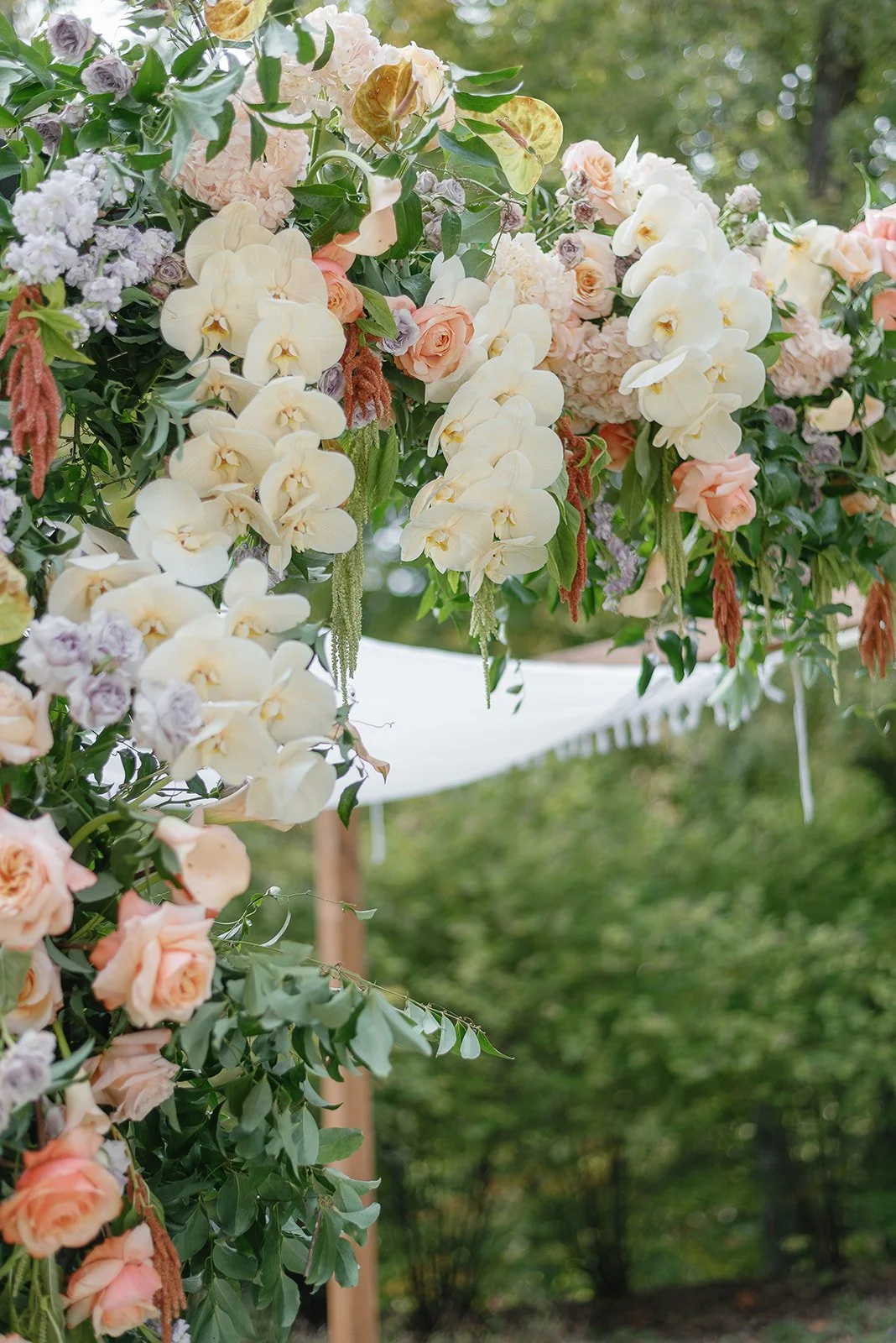Floral arrangement with white orchids, pink roses, green leaves, and purple flowers outdoors.