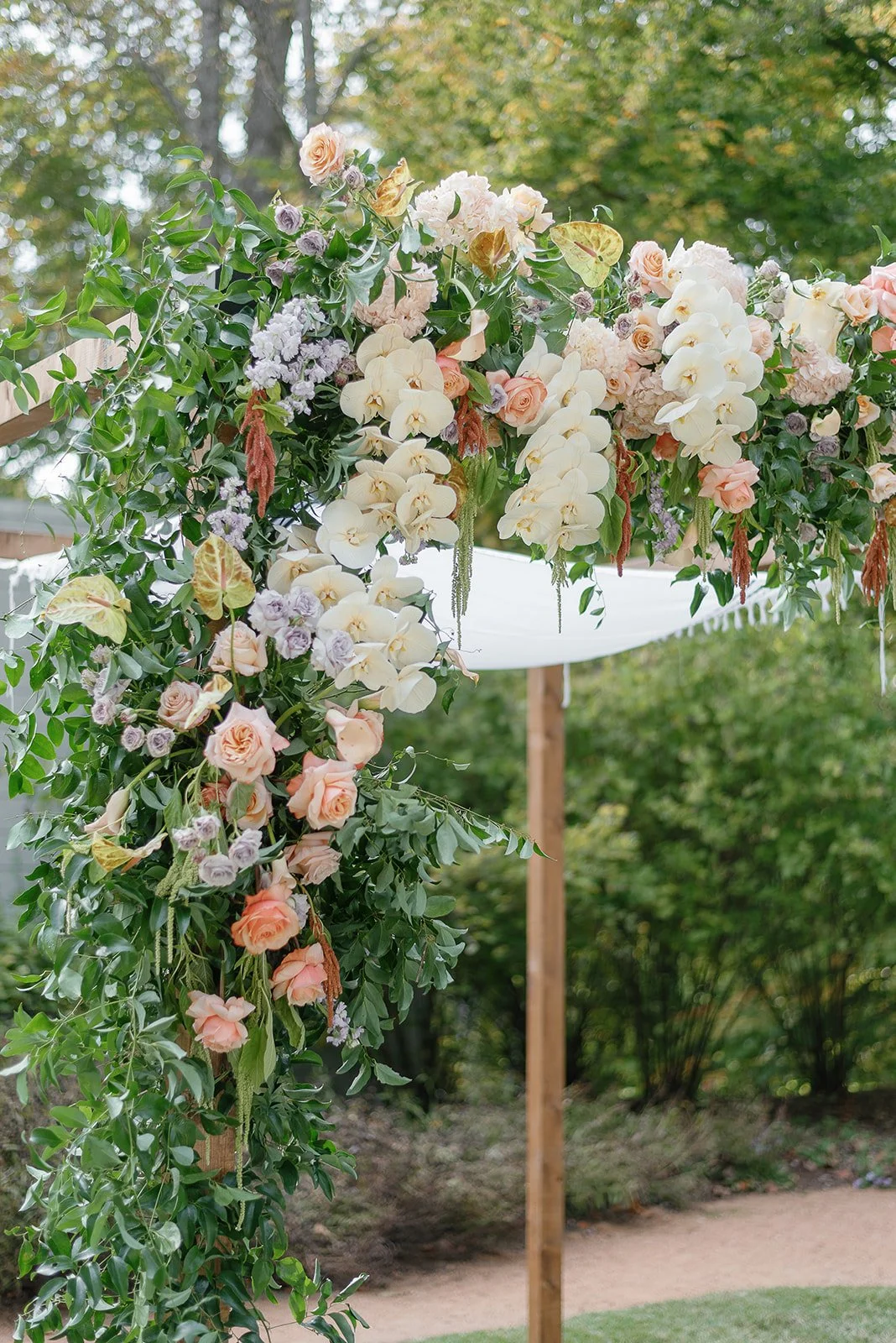 Wedding arch decorated with white orchids, pink roses, and greenery.