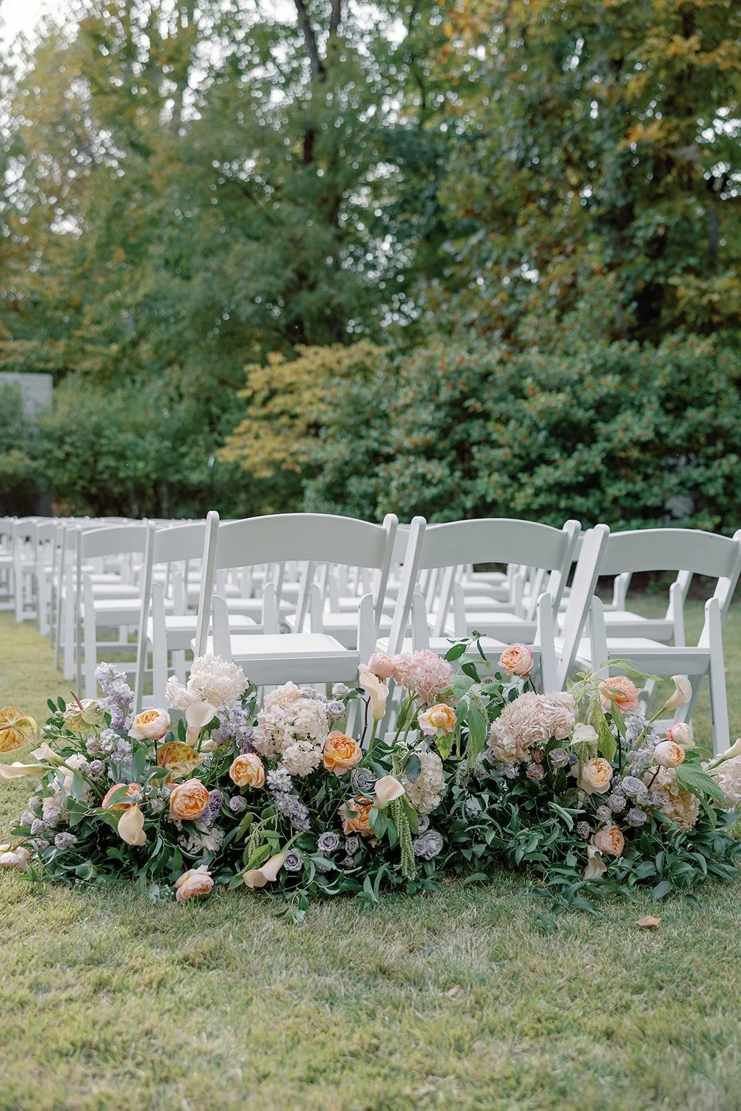 Outdoor wedding ceremony setup with white chairs and floral arrangements on a grassy area.