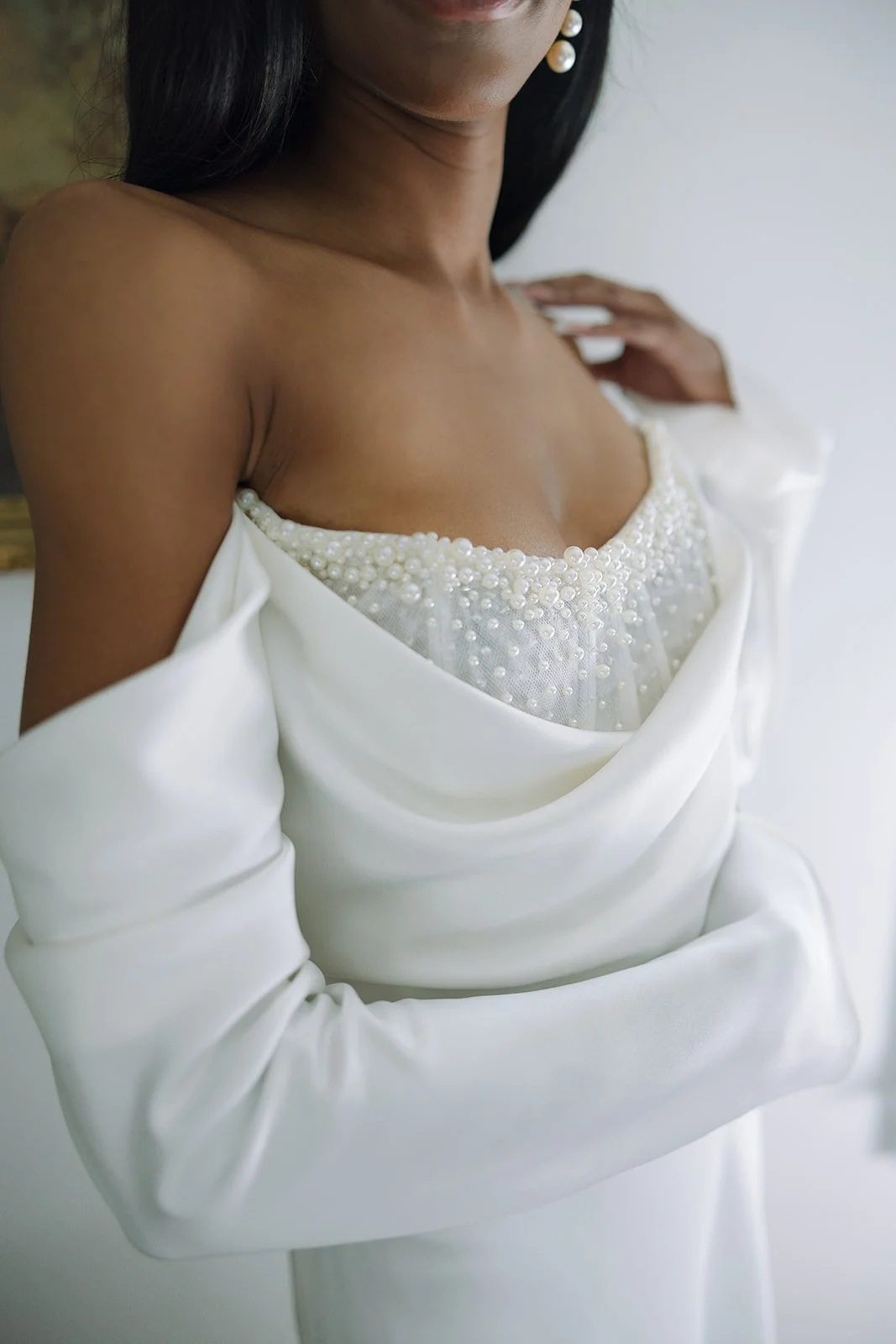 Close-up of a woman wearing an off-shoulder white dress with pearl embellishments, with long black hair and pearl earrings visible.