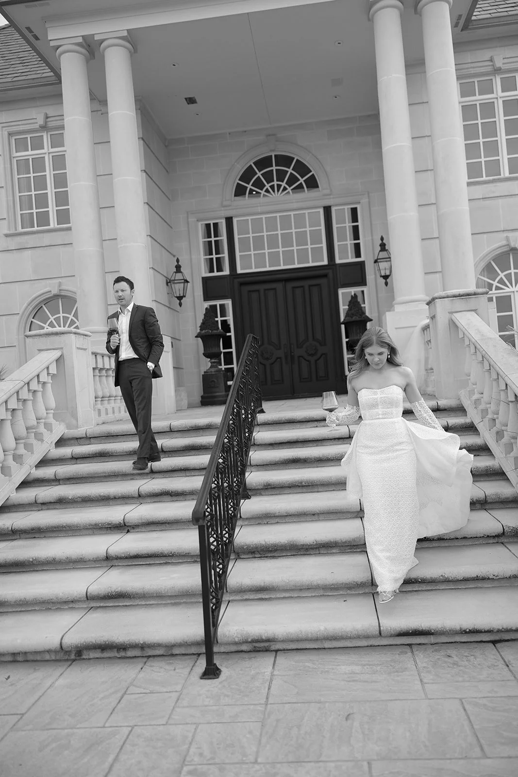 Black and white photo of a man and woman descending stone stairs in formal attire in front of a grand building with columns.