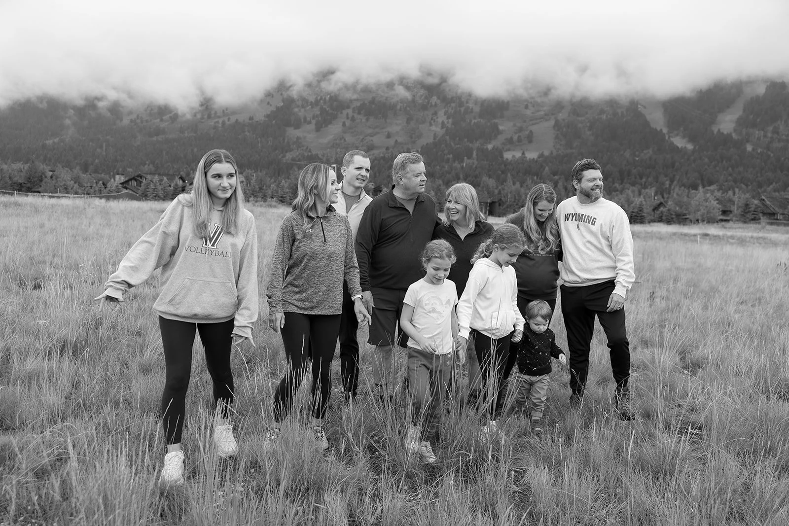A family group walking on a grassy field with mountains and cloudy sky in the background