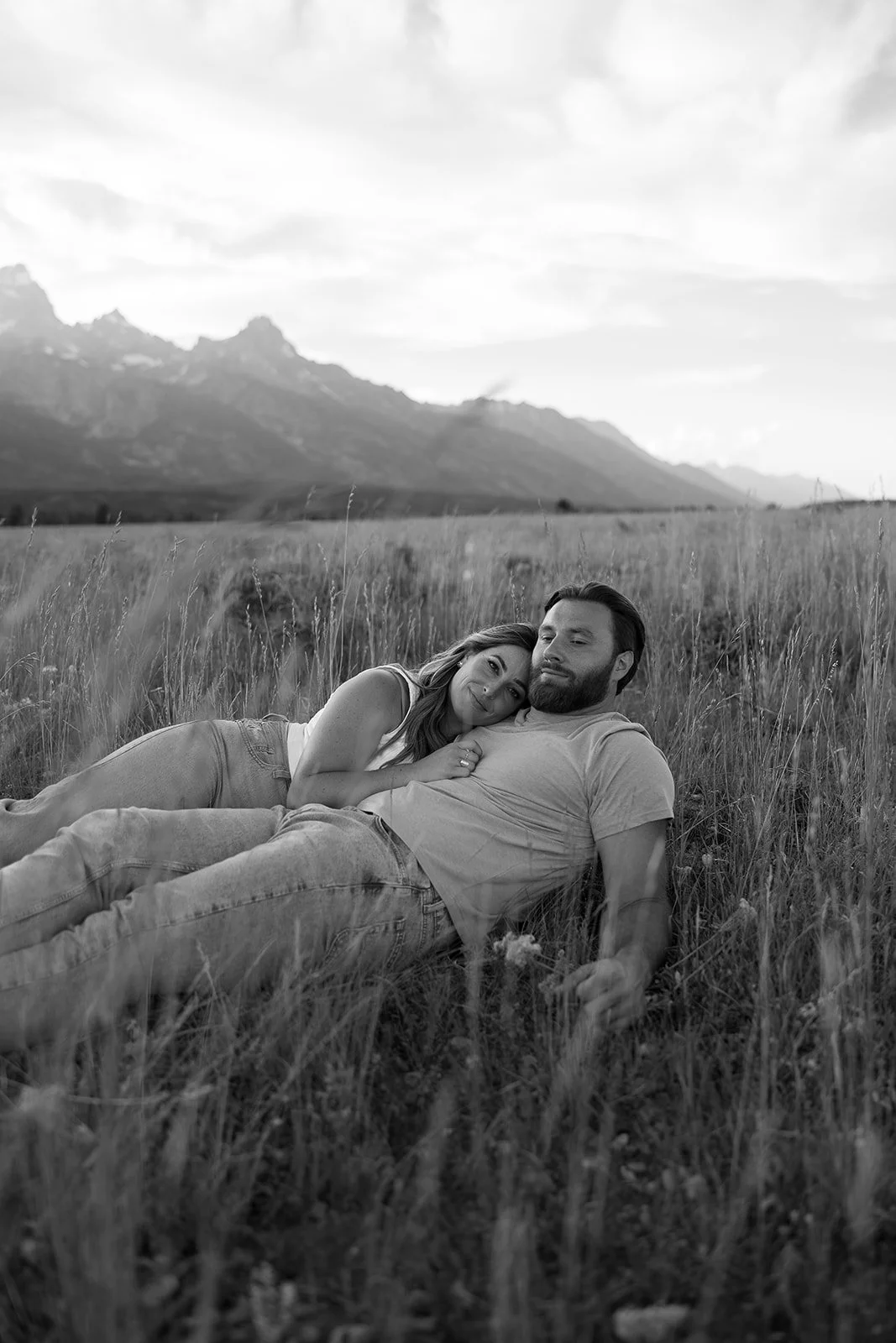 A couple lying on grass in a field with mountains in the background