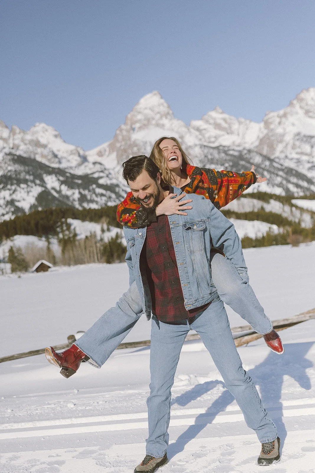 A couple playing in the snow with a scenic mountain range in the background.