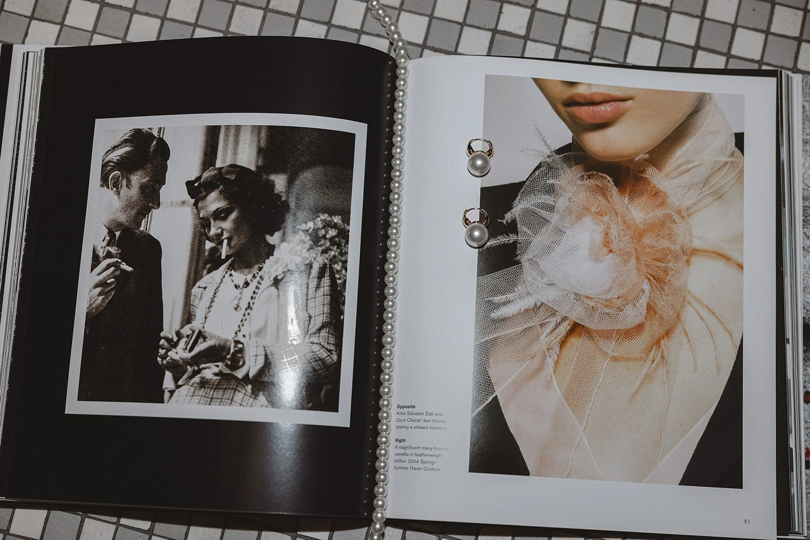 Open book with black-and-white photo on left of two people conversing, and color photo on right showing a close-up of a model wearing a tulle fashion accessory and pearl jewelry. A string of pearls lies across the pages.