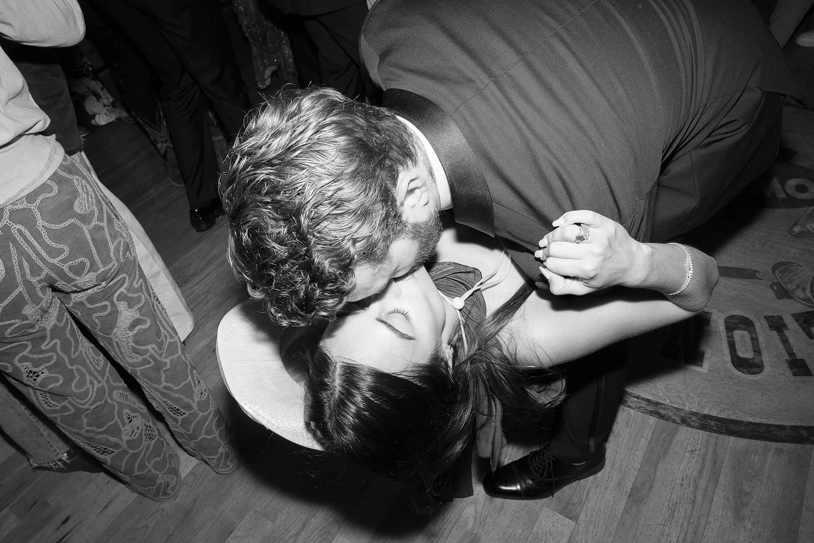 A man and woman dancing closely, with the man leaning over the woman, who is lying on her back. The woman has her eyes closed, and the scene appears to be at a social gathering or party.