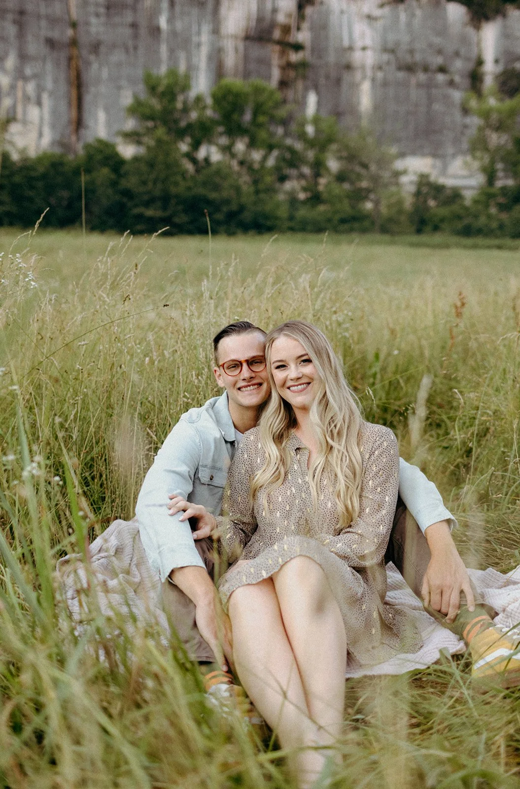 Couple sitting in a grassy field, smiling and embracing.