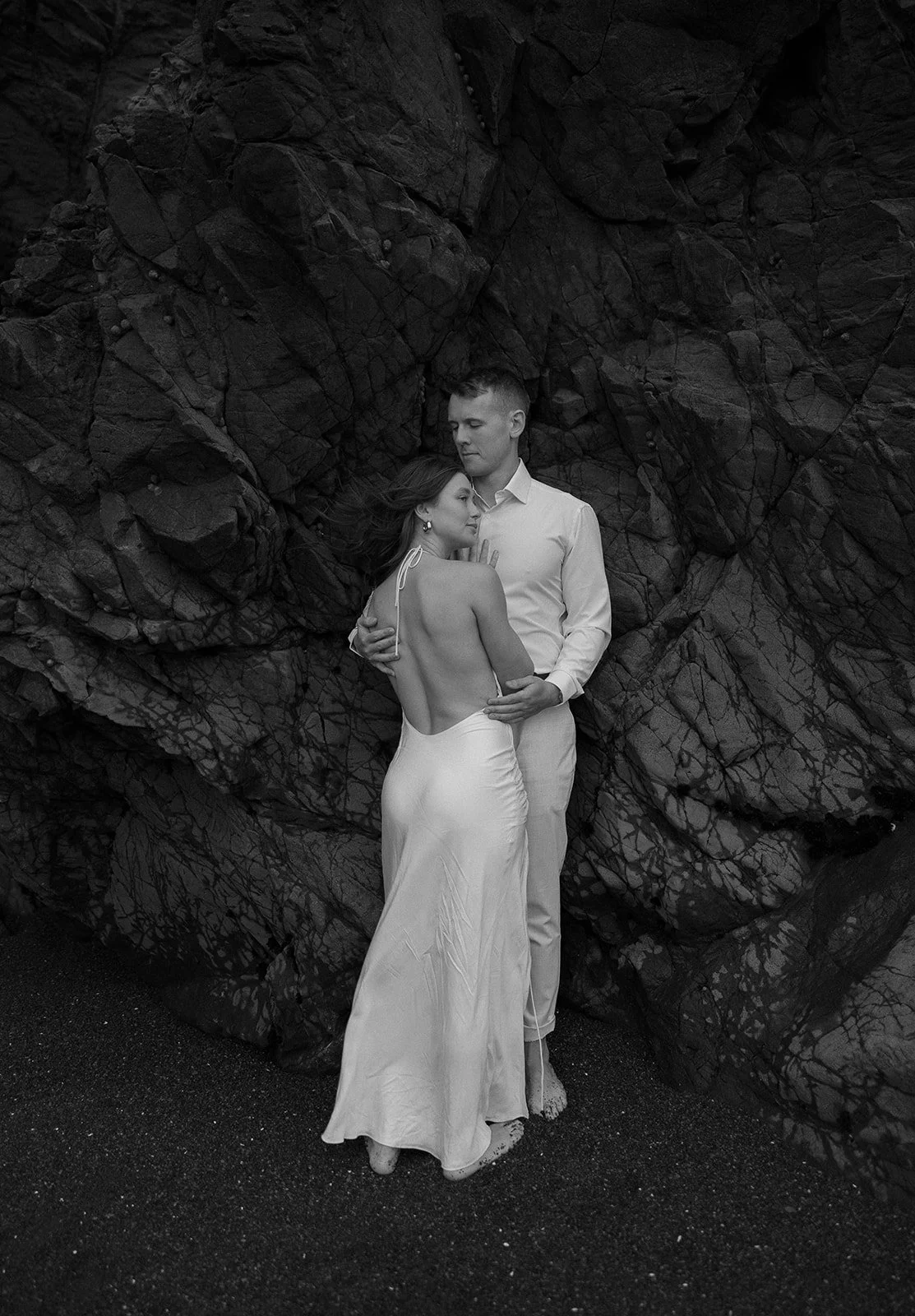 Black and white photo of a couple embracing against a rocky background.