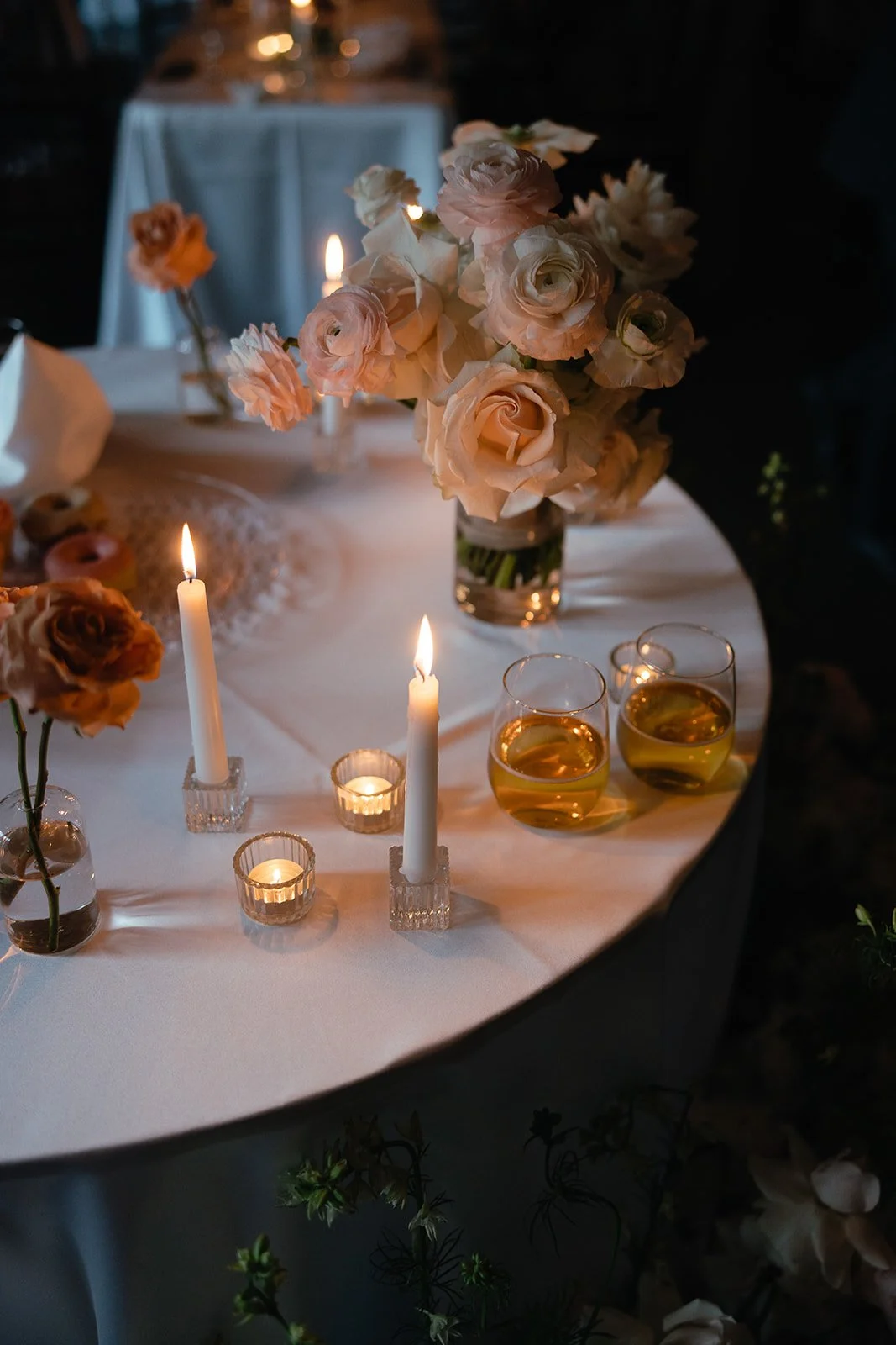 Elegant table setting with burning candles, roses, and two glasses of drink.