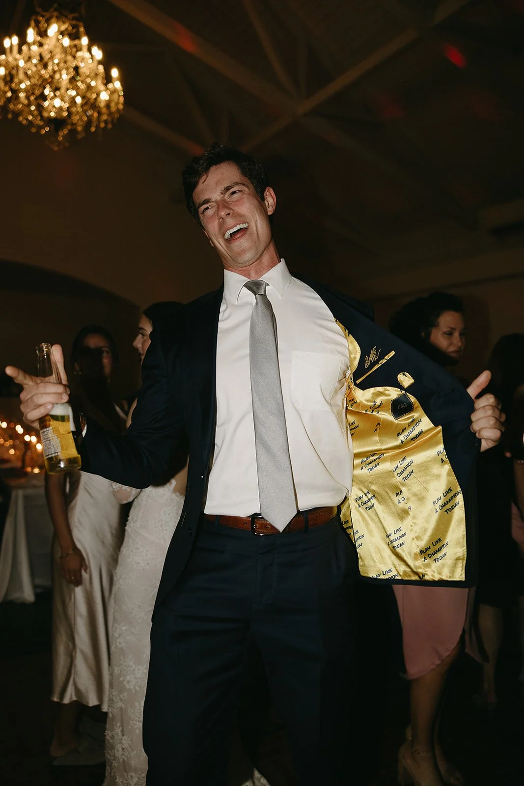 Man in suit with yellow lining holding a drink, smiling at a party.