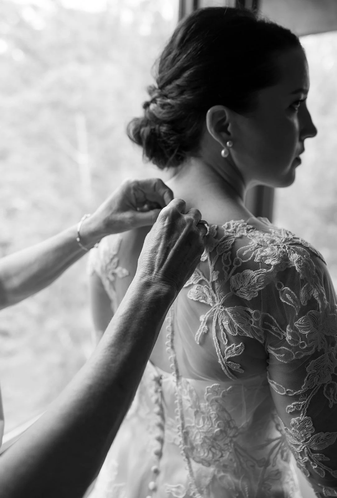 Woman in lace wedding dress getting buttoned by another person